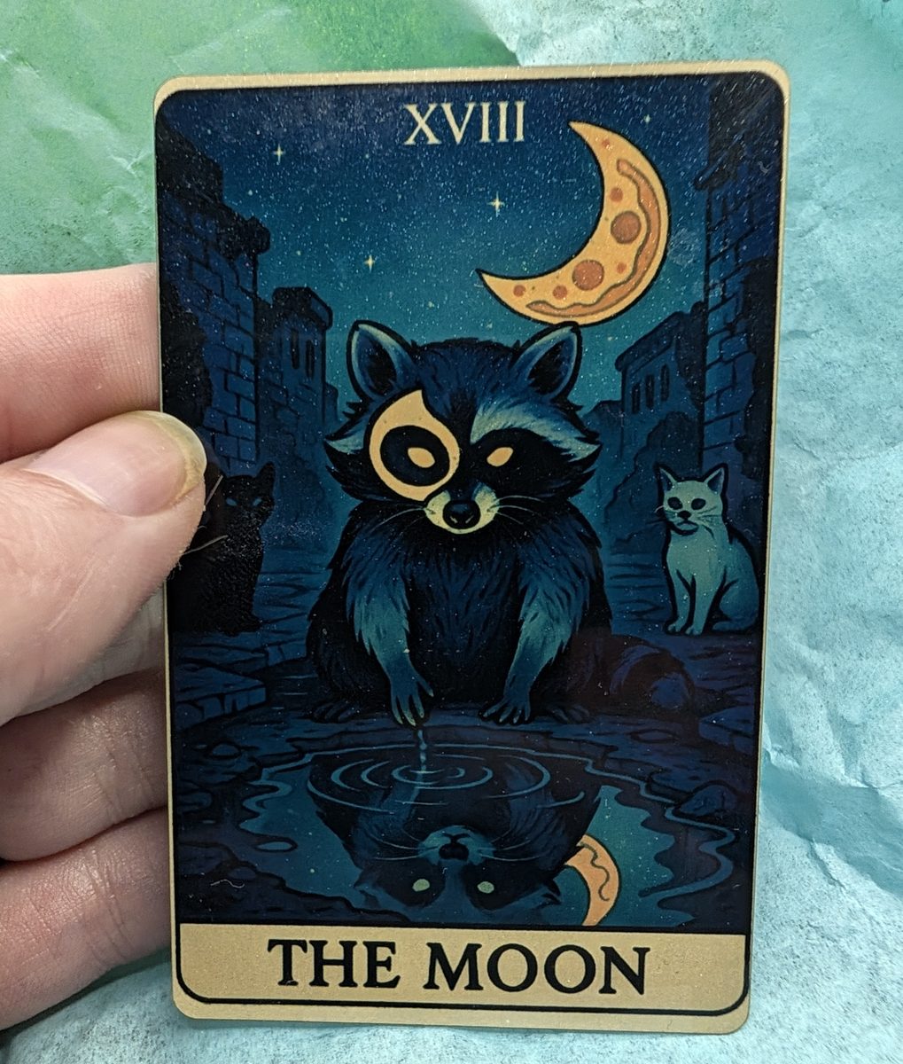 The Moon card from the Oracle of the Moonlit Dumpster deck held in hand: a raccoon sitting at a puddle in a dark alley under a crescent moon shaped like a slice of pizza