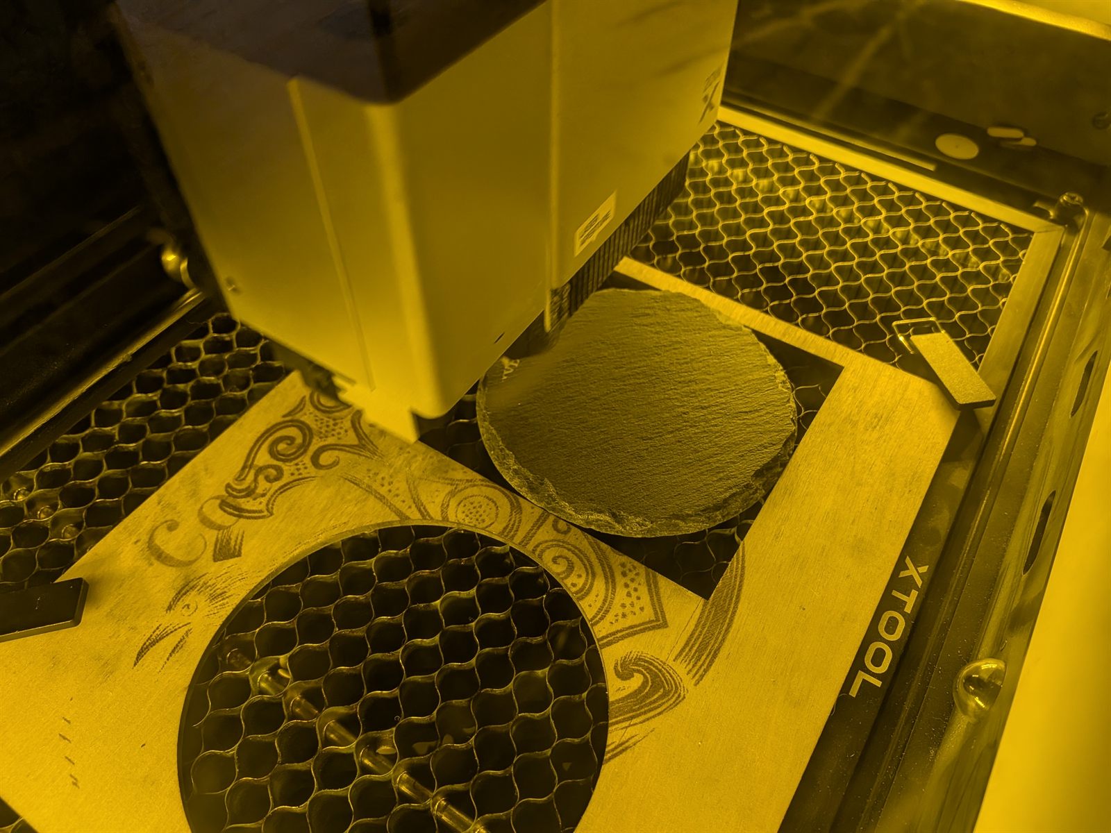 A slate coaster being laser engraved on the xTool, part of the Neurospice Design Shop production process