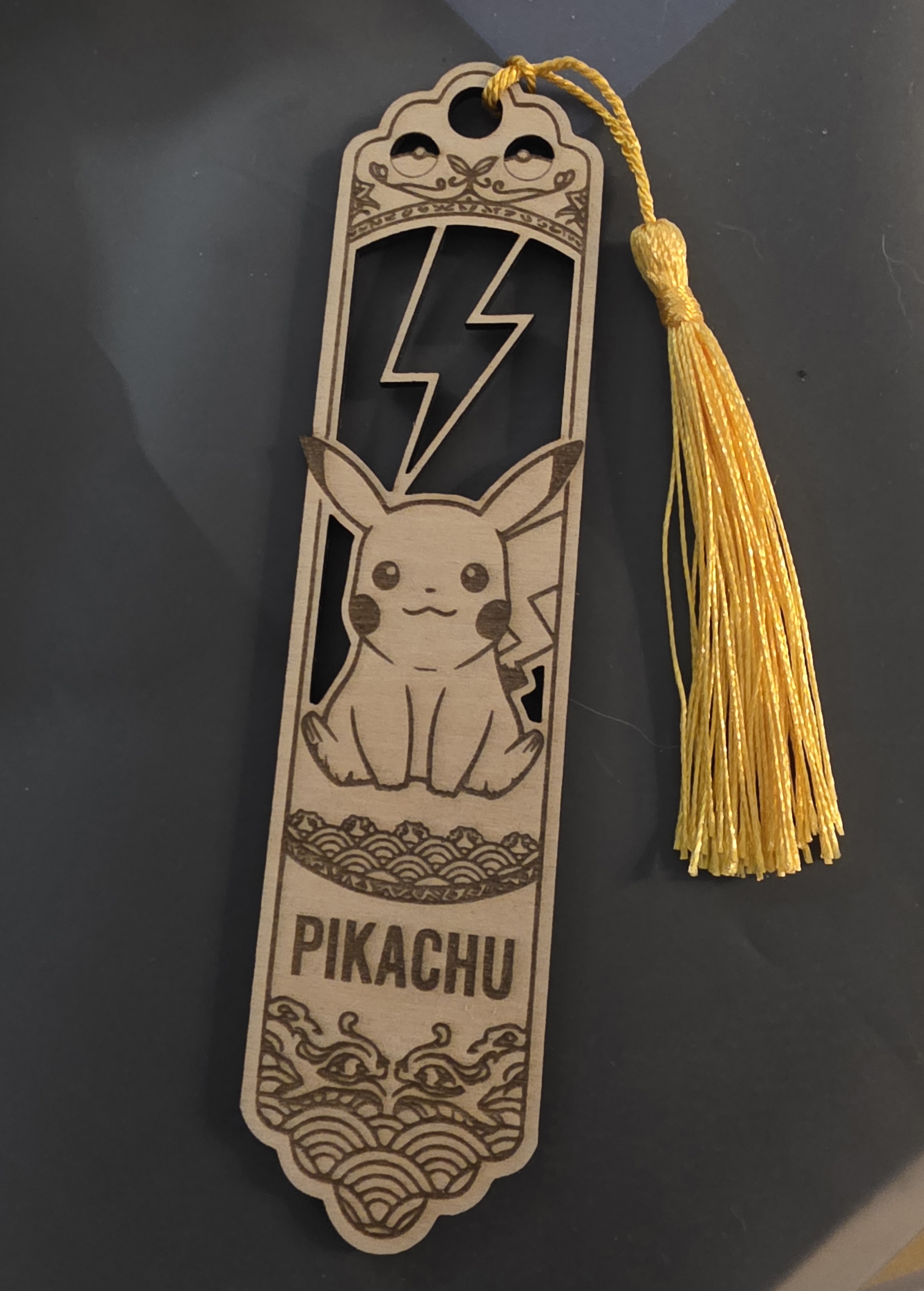 A laser-engraved Pikachu wooden bookmark with a yellow tassel, handmade for a kid's birthday